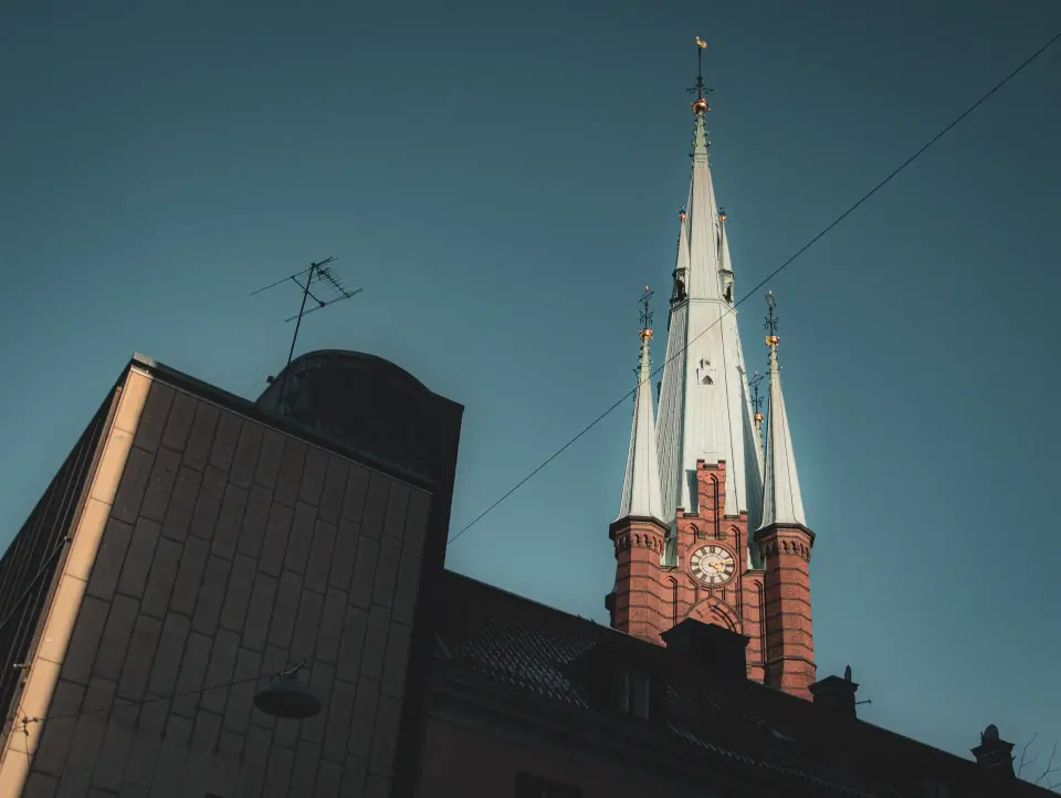 Chiesa con guglie illuminate vista tra edifici urbani.