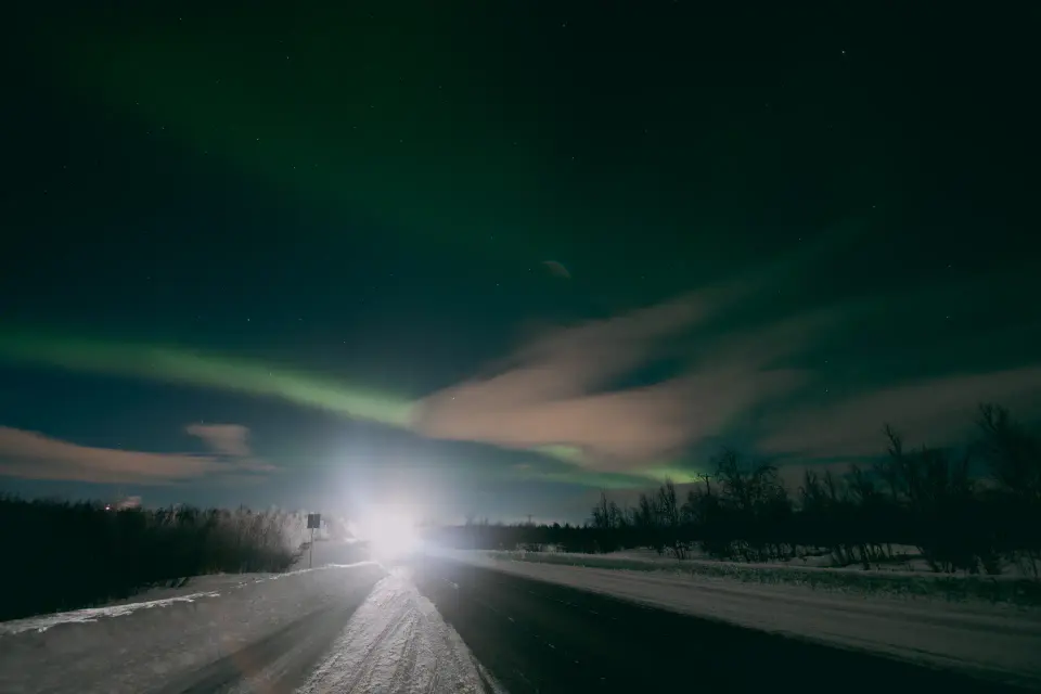 Strada notturna con luce centrale e cielo verdastro.