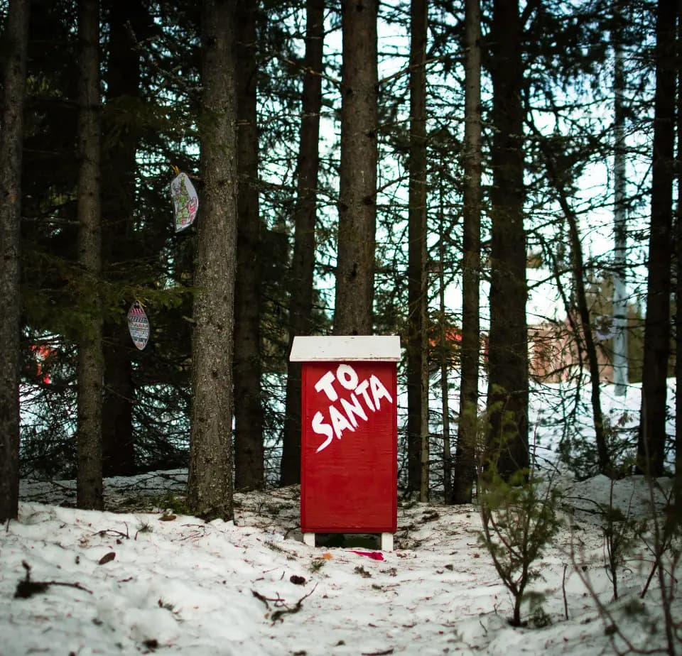 Cabina telefonica rossa in un bosco innevato.