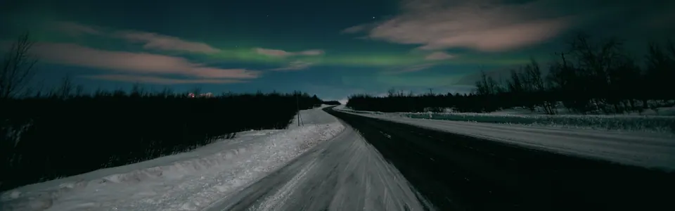 Strada vuota in notturna con bagliore all'orizzonte.